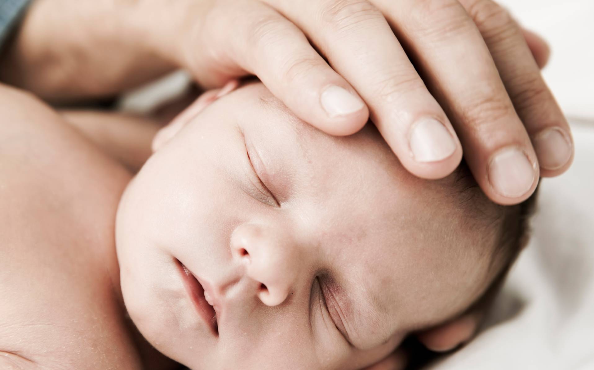 photographie d'un nourrisson qui reçoit les caresses d'un de ses parents